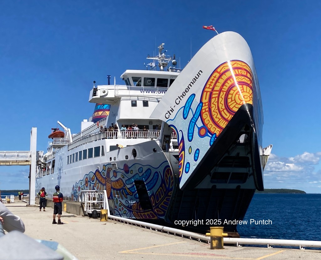 The colourfully painted passenger/car ferry Chi-Cheemaun, with its front brow opening up, approaches the loading dock at Tobermory, Ontario.